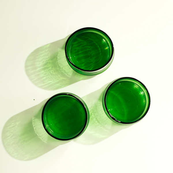 Three green tinted glass cups arranged on a white background, casting soft shadows.