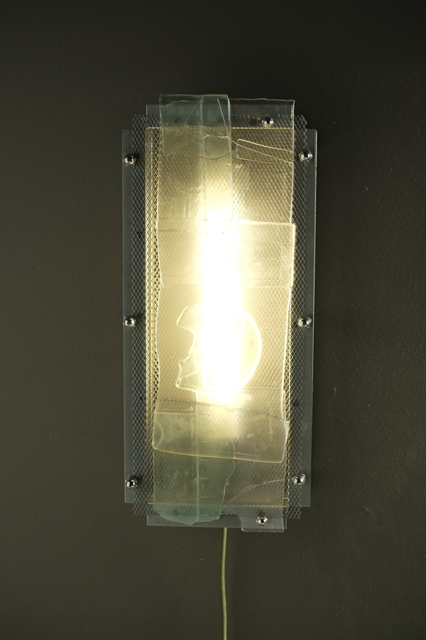 A rectangular wall-mounted light fixture with a glowing warm white bulb inside a clear textured glass panel, mounted on a dark wall.