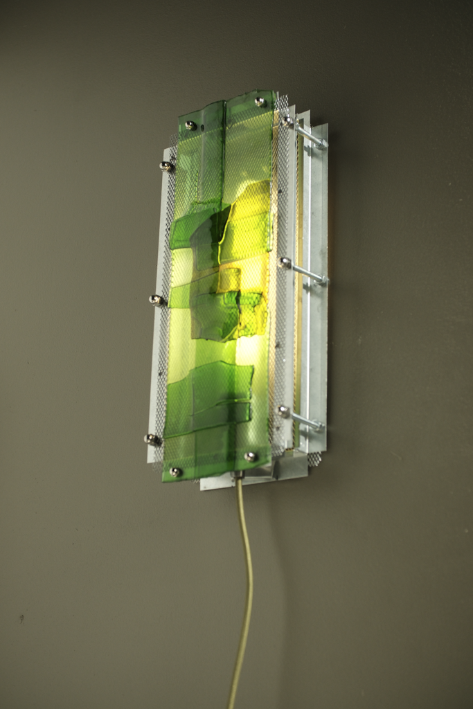 A modern wall-mounted light fixture with translucent green and yellow acrylic panels set in a silver metal frame, shown mounted on a dark gray wall.